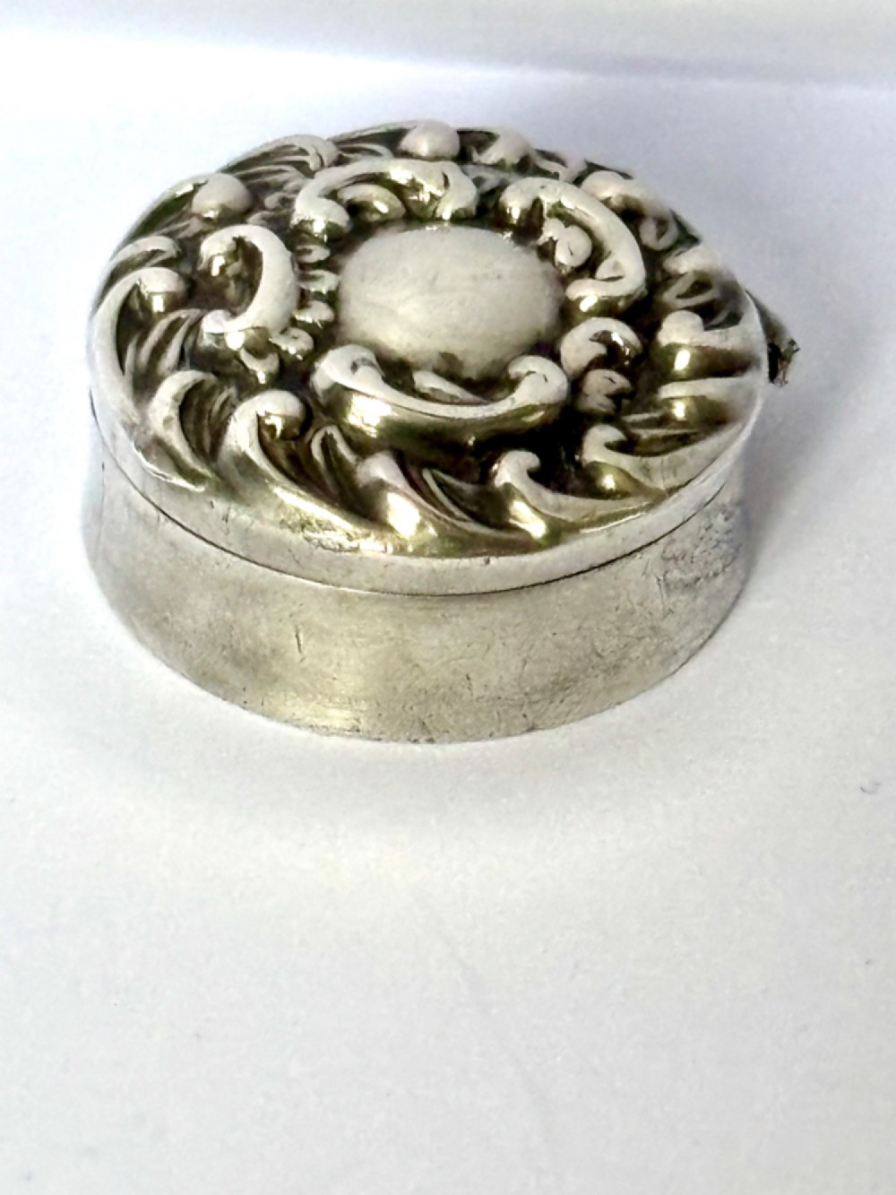 A small circular Edwardian sterling silver gilt trinket box with embossed scrollwork decoration on the lid. View IV