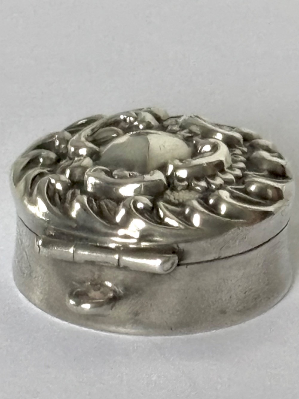 A small circular Edwardian sterling silver gilt trinket box with embossed scrollwork decoration on the lid. View VI