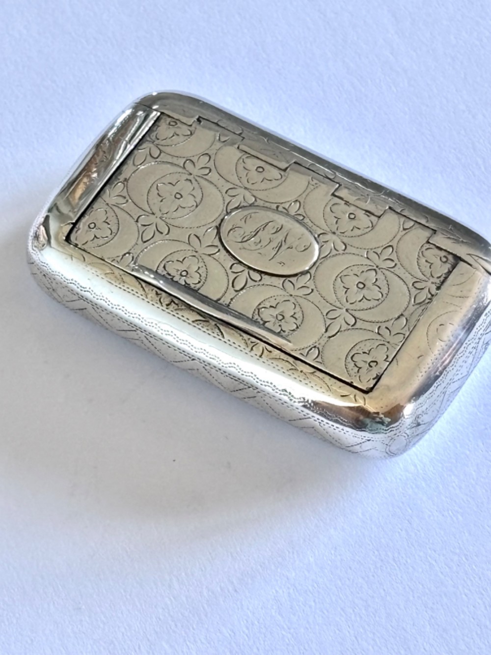A small rectangular George III sterling silver snuff box with bright-cut floral engraving and a central oval cartouche.