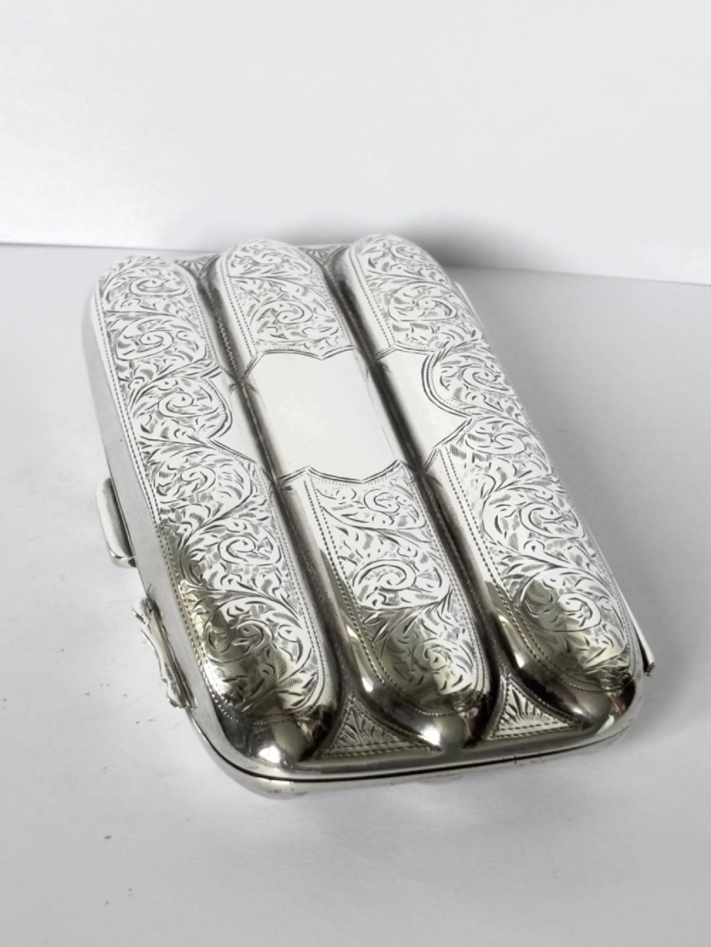 An Edwardian sterling silver triple cigar case featuring engraved foliate scrollwork and three rounded channels. View II