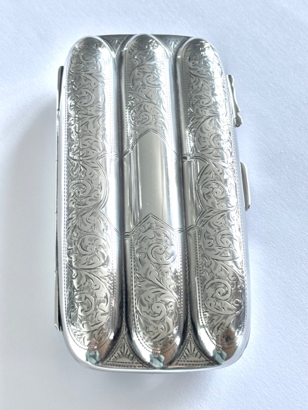 An Edwardian sterling silver triple cigar case featuring engraved foliate scrollwork and three rounded channels. View III
