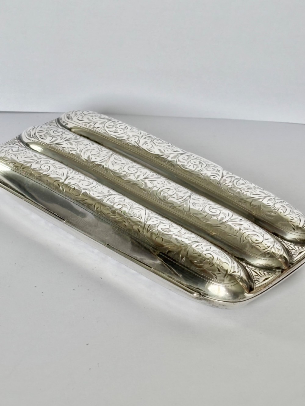 An Edwardian sterling silver triple cigar case featuring engraved foliate scrollwork and three rounded channels. View IV