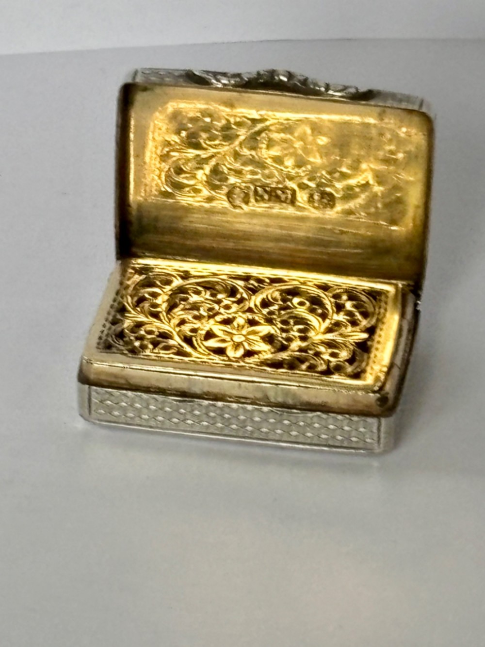 A small open rectangular silver-gilt box featuring a finely pierced floral inner grille and engraved lid detailing.