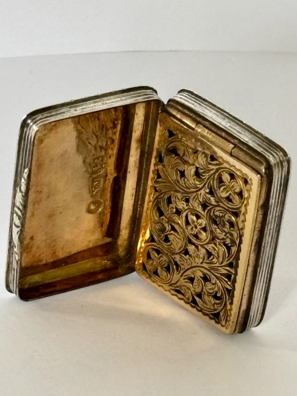 An open Early Victorian silver gilt vinaigrette showing a floral pierced interior grille and hallmarks on the inside lid. View VII