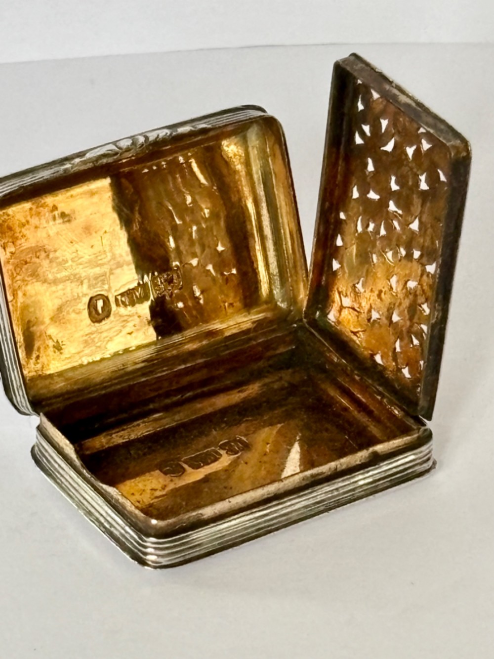 An open Early Victorian silver gilt vinaigrette showing a floral pierced interior grille and hallmarks on the inside lid. View VIII