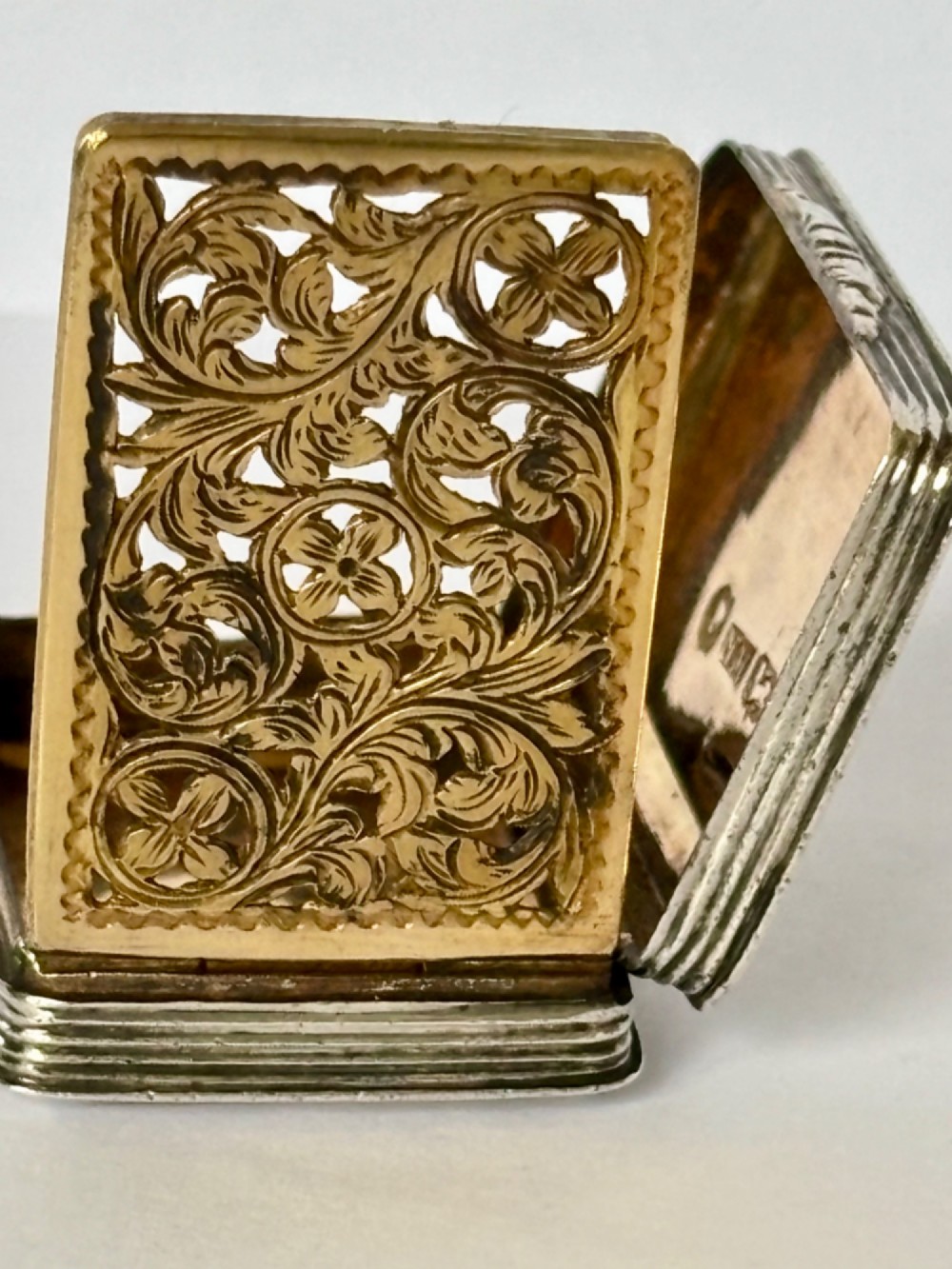 An open Early Victorian silver gilt vinaigrette showing a floral pierced interior grille and hallmarks on the inside lid. View IX