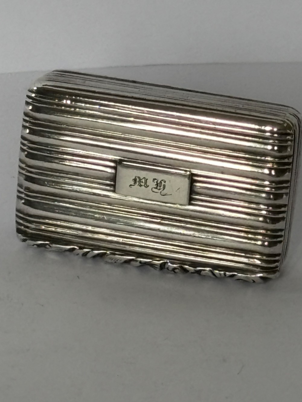 An open George IV rectangular silver-gilt vinaigrette showing internal hallmarks and a hinged pierced grille next to a small dark sponge. View II