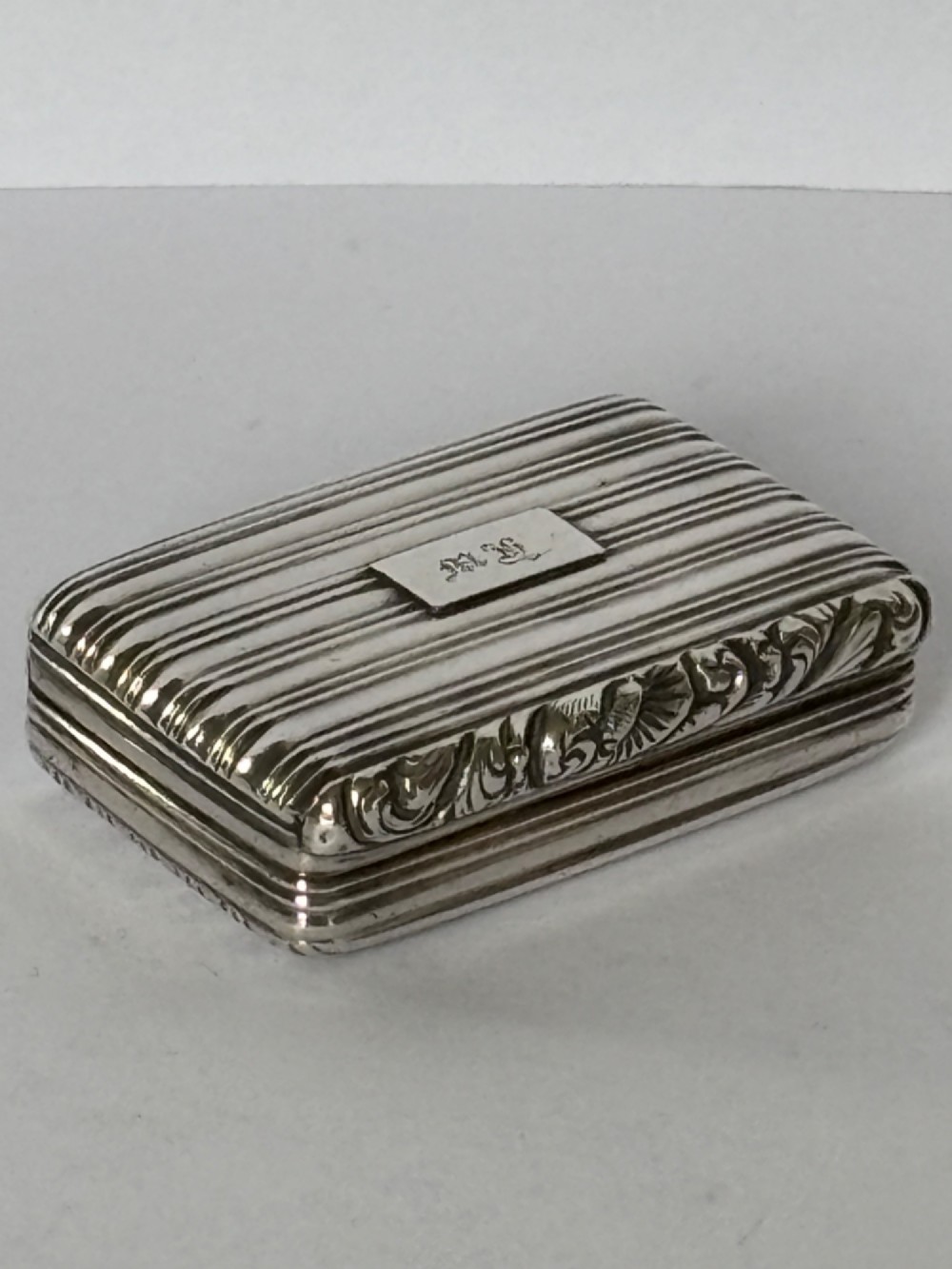 An open George IV rectangular silver-gilt vinaigrette showing internal hallmarks and a hinged pierced grille next to a small dark sponge. View III