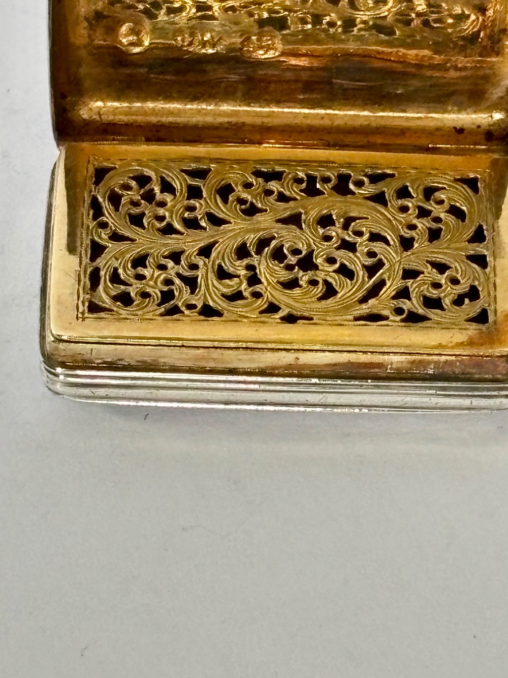 An open George IV rectangular silver-gilt vinaigrette showing internal hallmarks and a hinged pierced grille next to a small dark sponge. View V