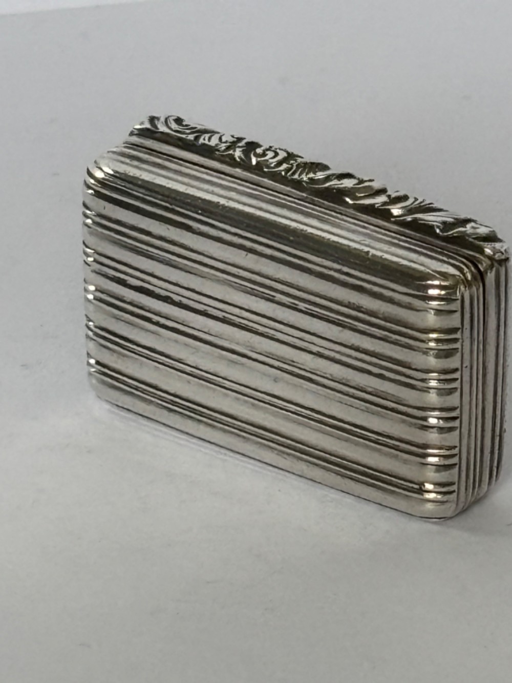 An open George IV rectangular silver-gilt vinaigrette showing internal hallmarks and a hinged pierced grille next to a small dark sponge. View IX