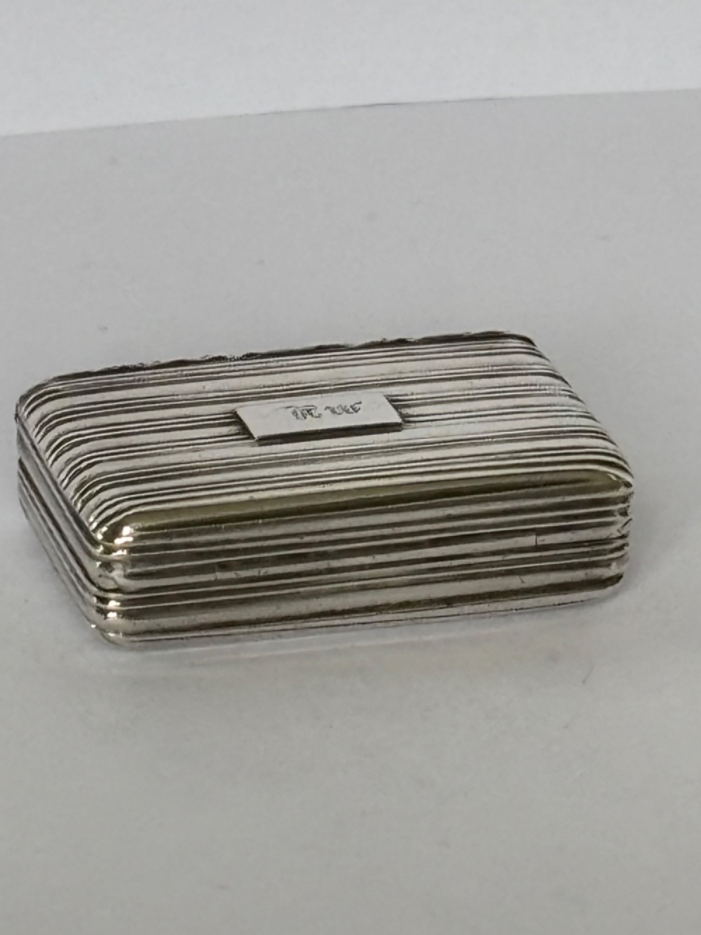 An open George IV rectangular silver-gilt vinaigrette showing internal hallmarks and a hinged pierced grille next to a small dark sponge. View X