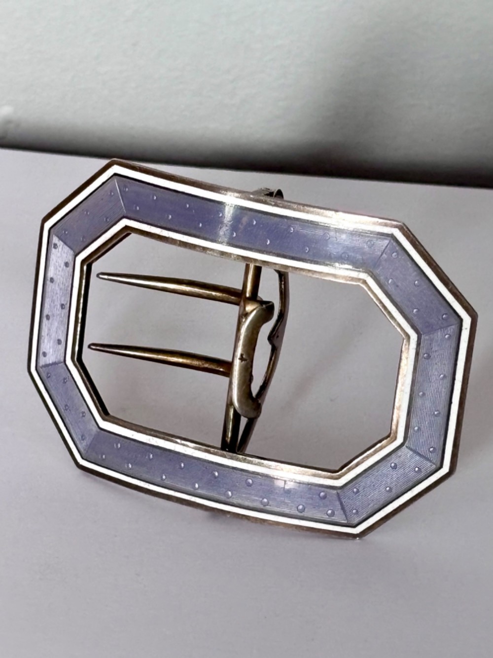 An octagonal antique silver belt buckle featuring lavender guilloche enamel bordered in white enamel with a central metal prong mechanism.
