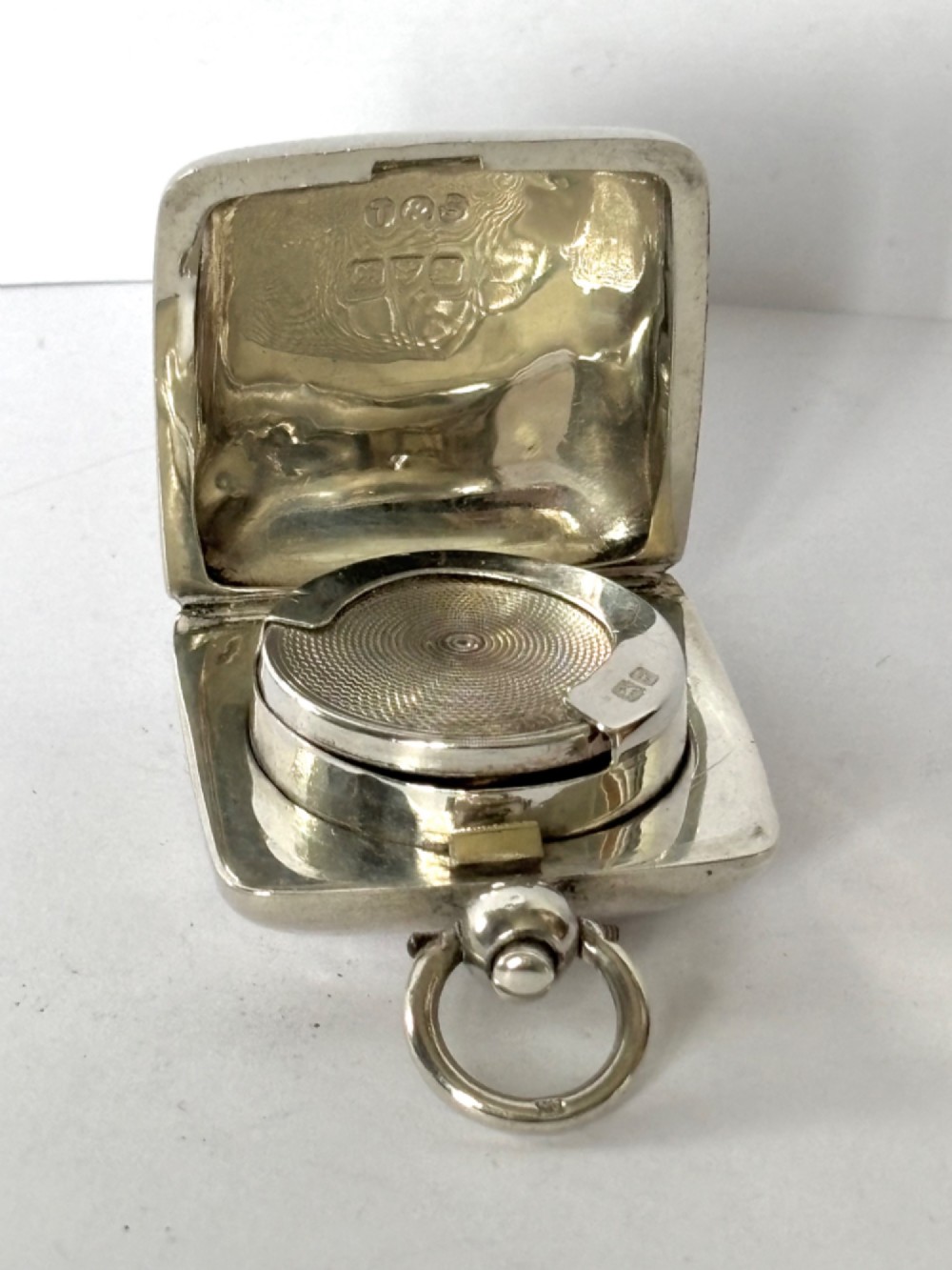 An open Edwardian square sterling silver sovereign case featuring a spring-loaded coin holder and stamped hallmarks on the interior lid.