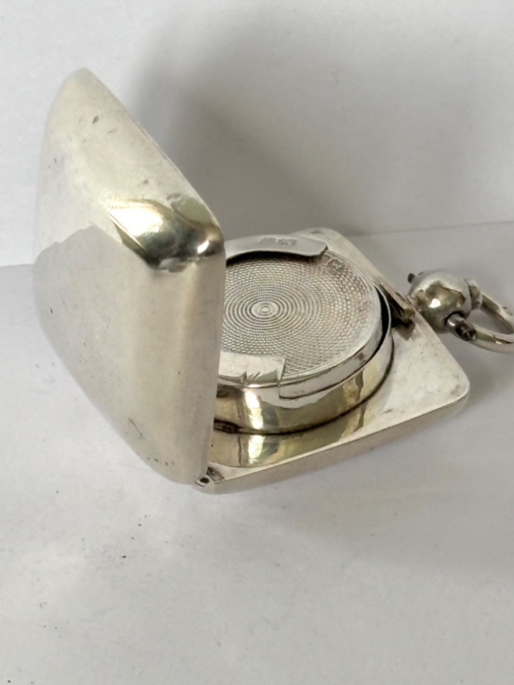 An open Edwardian square sterling silver sovereign case featuring a spring-loaded coin holder and stamped hallmarks on the interior lid. View III