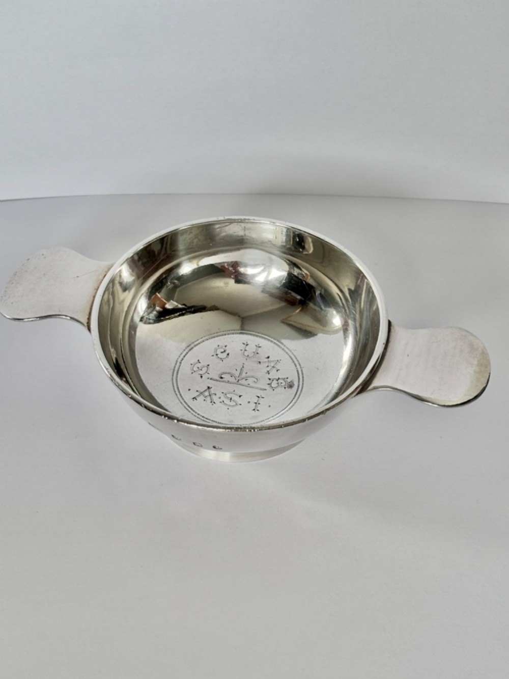 A shallow sterling silver Scottish quaich featuring two flat lug handles and engraved Gaelic lettering in the centre bowl.