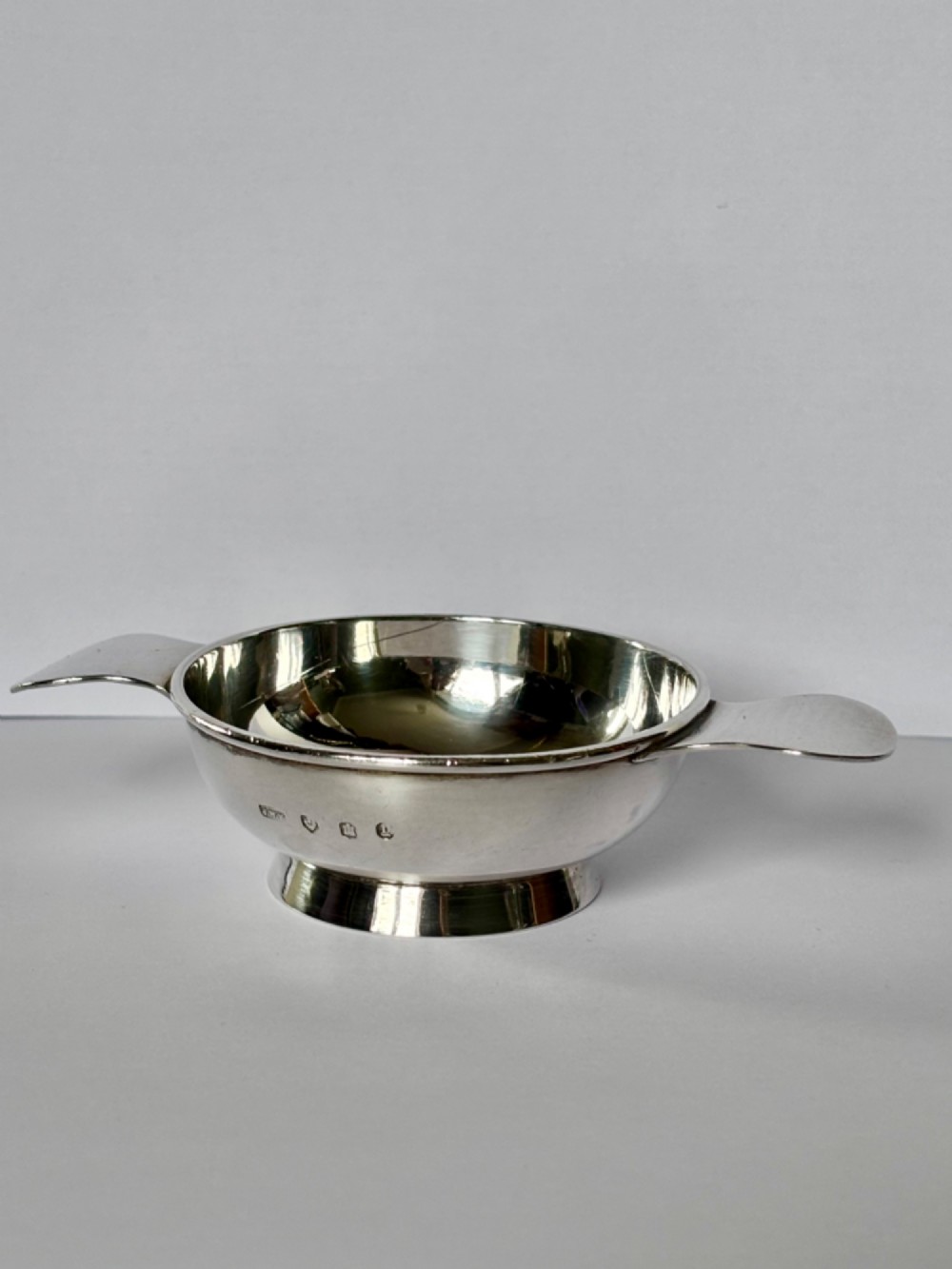 A shallow sterling silver Scottish quaich featuring two flat lug handles and engraved Gaelic lettering in the centre bowl. View III