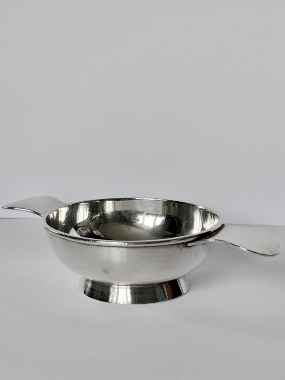 A shallow sterling silver Scottish quaich featuring two flat lug handles and engraved Gaelic lettering in the centre bowl. View VI