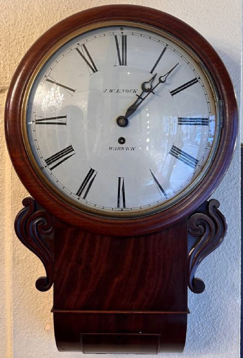 fig 1. A nineteenth-century mahogany drop-dial wall clock with a circular white dial, black Roman numerals, brass bezel, and carved side scrolls.