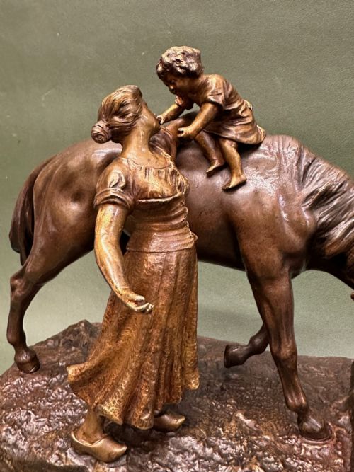 fig 1. A patinated bronze sculpture depicting a mother and child standing beside a horse drinking from a trough, mounted on a pink veined marble base.