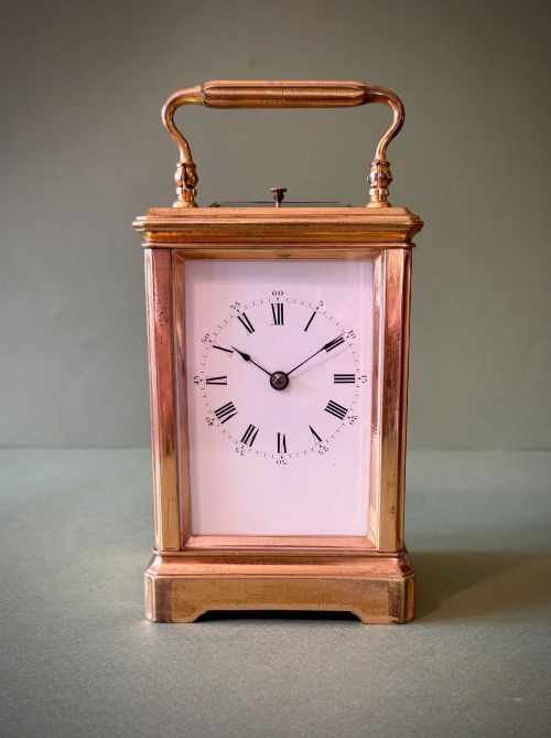 fig 1. A 19th-century French gilt brass carriage clock with bevelled glass side panels, an enamel dial with Roman numerals, and a hinged top carrying handle.