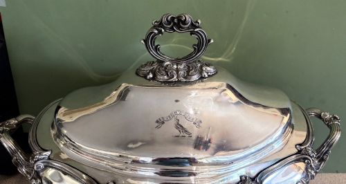 fig 1. An antique silver-plated three-piece soup tureen featuring a domed lid with a scroll handle, engraved heraldic crest, and ornate scrolled feet.
