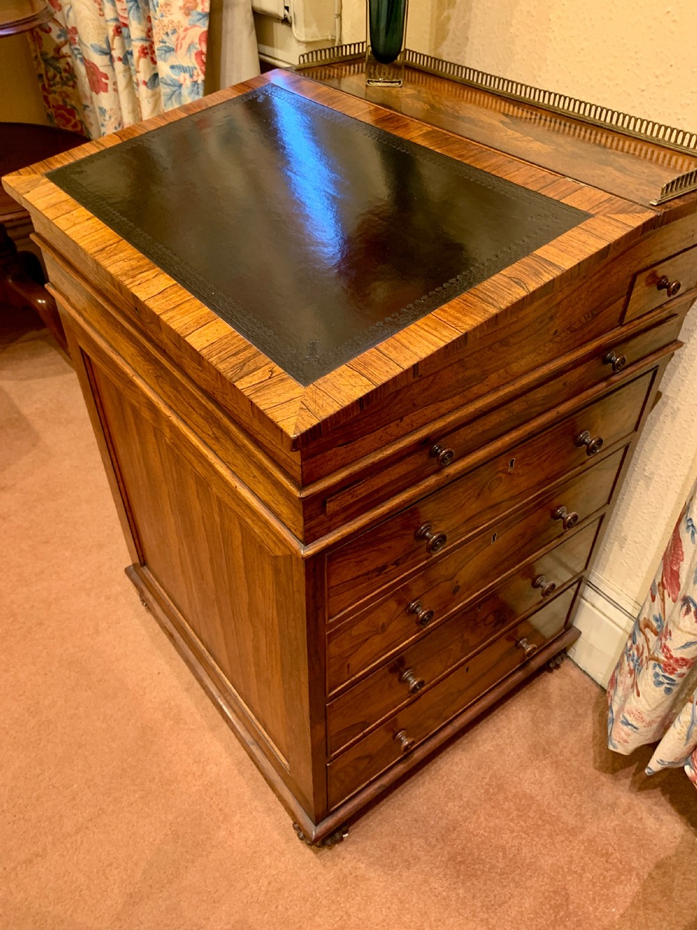 An antique rosewood Davenport desk featuring a sloped leather writing surface, top brass gallery, and side drawers with turned wooden knobs.