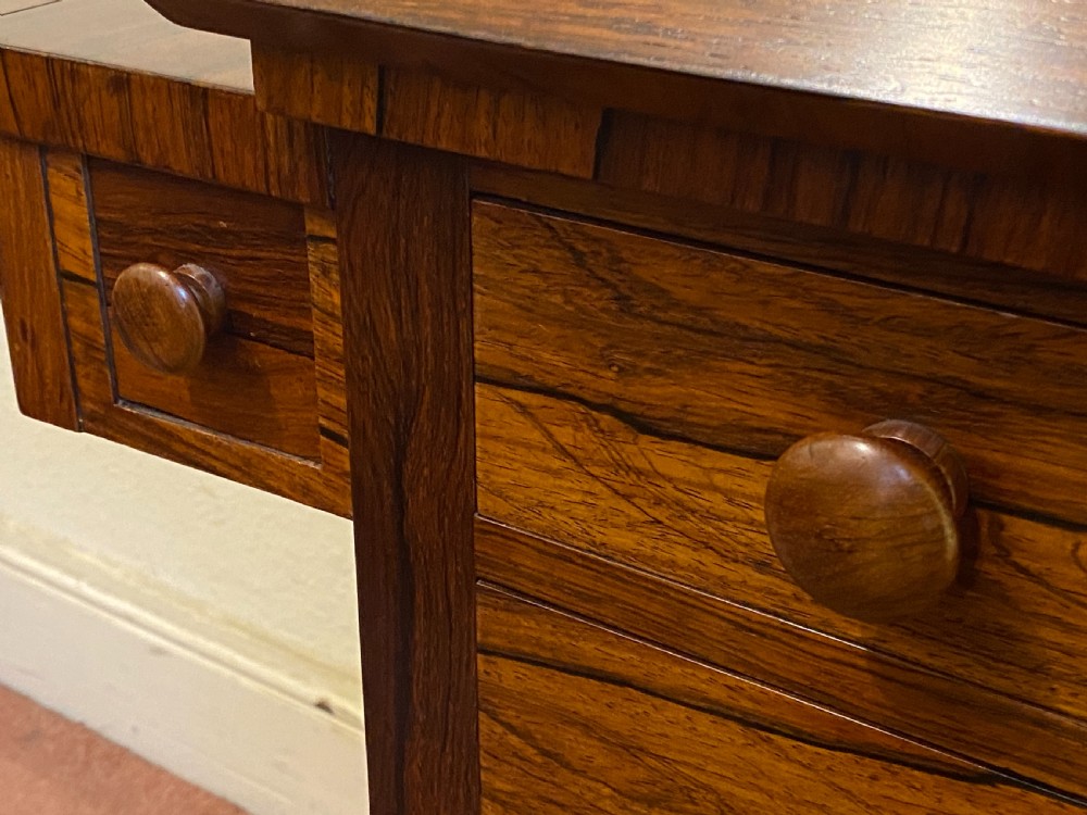 A William IV rosewood writing and work table featuring an adjustable leather-inset writing slope, drop-leaf sides, two drawers, and reeded turned legs on brass castors. View XVI