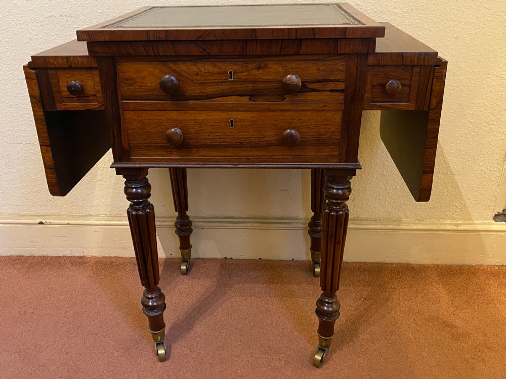 A William IV rosewood writing and work table featuring an adjustable leather-inset writing slope, drop-leaf sides, two drawers, and reeded turned legs on brass castors. View XXI