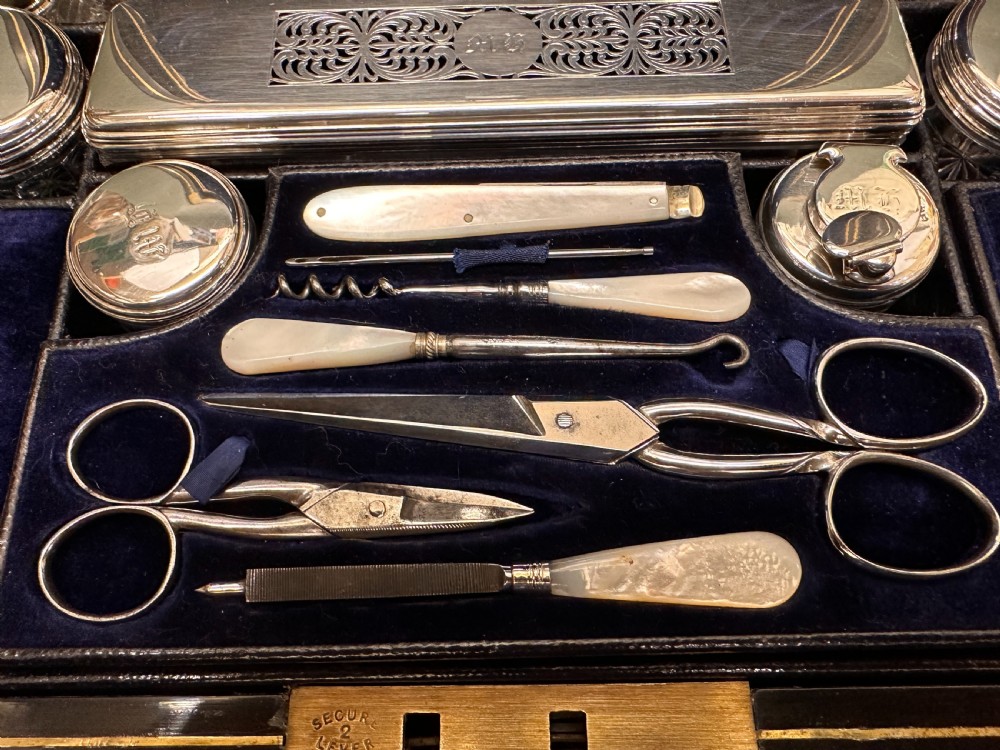 An open 19th-century kingwood dressing case with brass inlay, lined in blue velvet and fitted with silver-topped glass bottles, silver containers, and manicure tools. View XIX