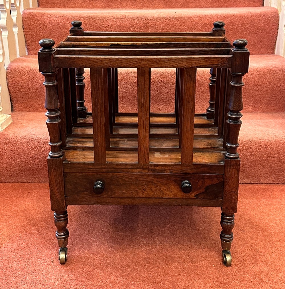 A 19th-century mahogany music Canterbury featuring four divided compartments, turned corner posts with finials, a single lower drawer with wooden knobs, and turned legs on brass castors.