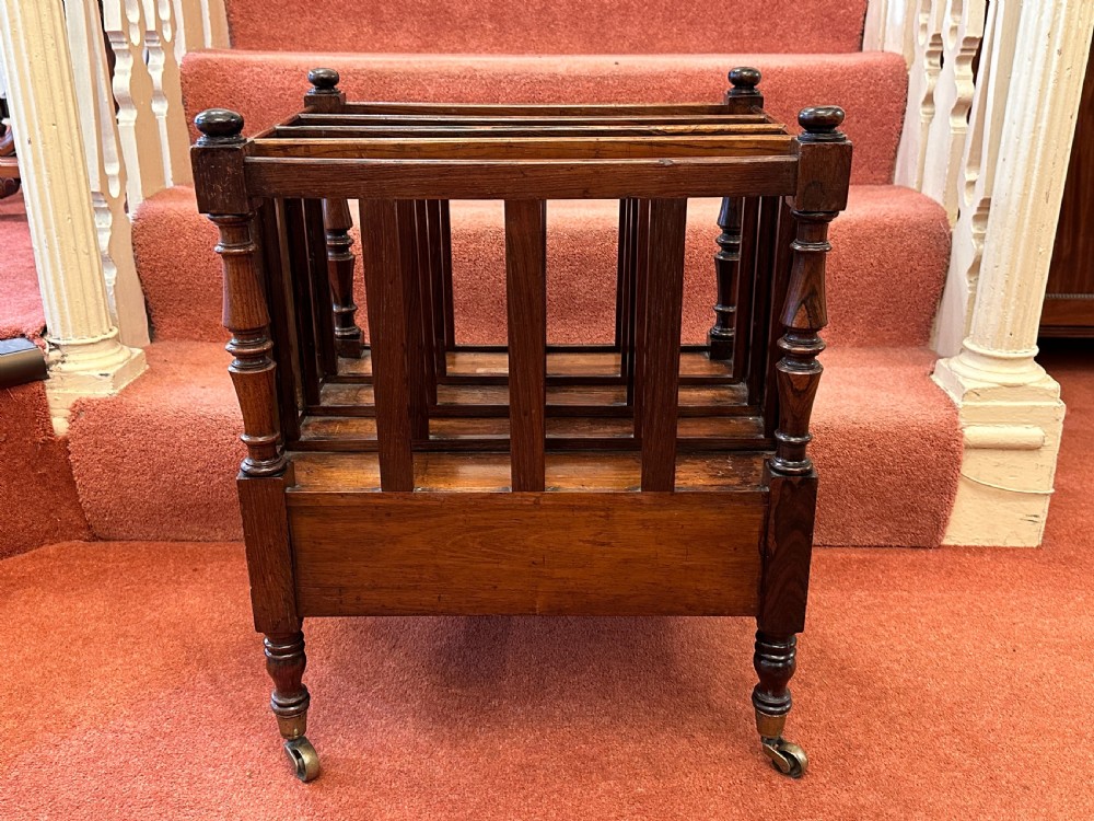 A 19th-century mahogany music Canterbury featuring four divided compartments, turned corner posts with finials, a single lower drawer with wooden knobs, and turned legs on brass castors. View V