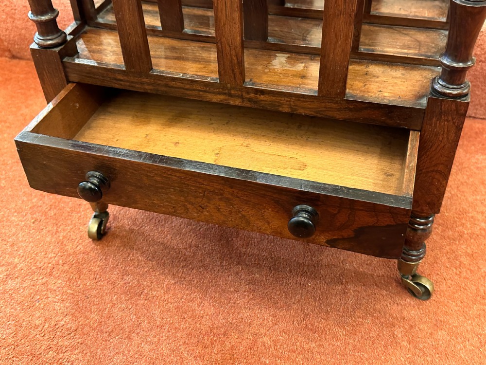 A 19th-century mahogany music Canterbury featuring four divided compartments, turned corner posts with finials, a single lower drawer with wooden knobs, and turned legs on brass castors. View VII