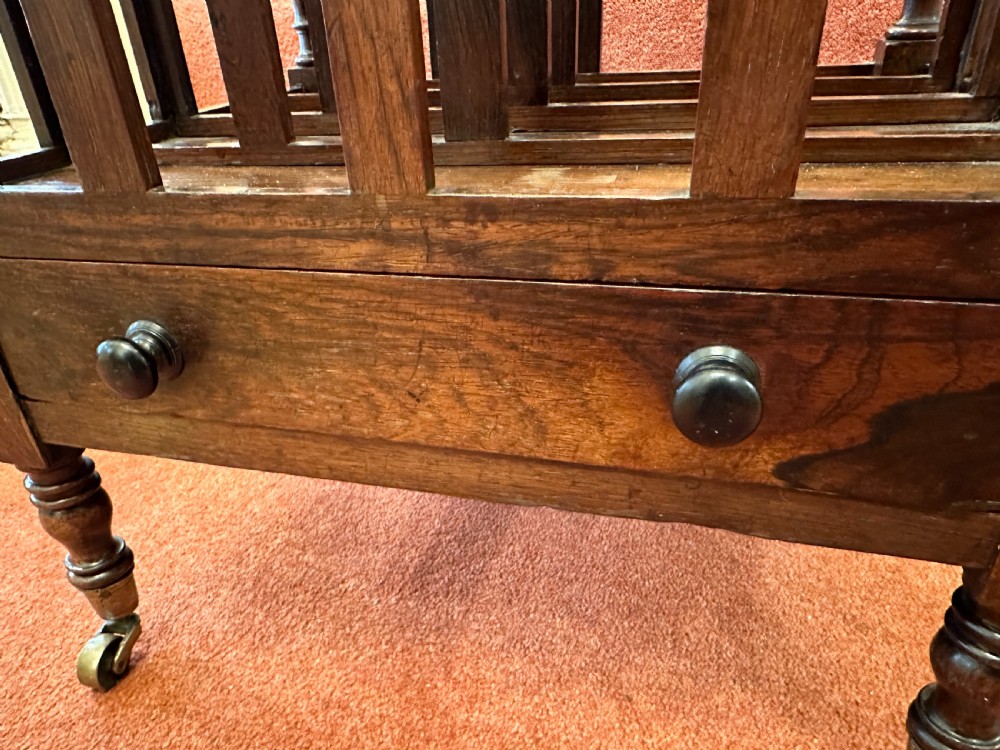 A 19th-century mahogany music Canterbury featuring four divided compartments, turned corner posts with finials, a single lower drawer with wooden knobs, and turned legs on brass castors. View X