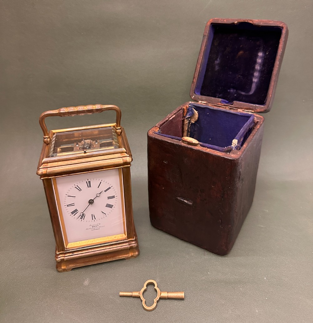 A Victorian gilt brass carriage clock with a white enamel dial next to its leather travelling box and double-ended winding key.