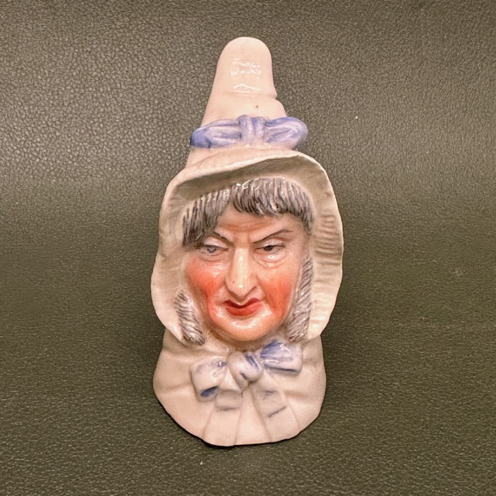 An 1893 Royal Worcester porcelain candle extinguisher sculpted in the likeness of Mrs Caudle wearing a white bonnet with a blue ribbon.