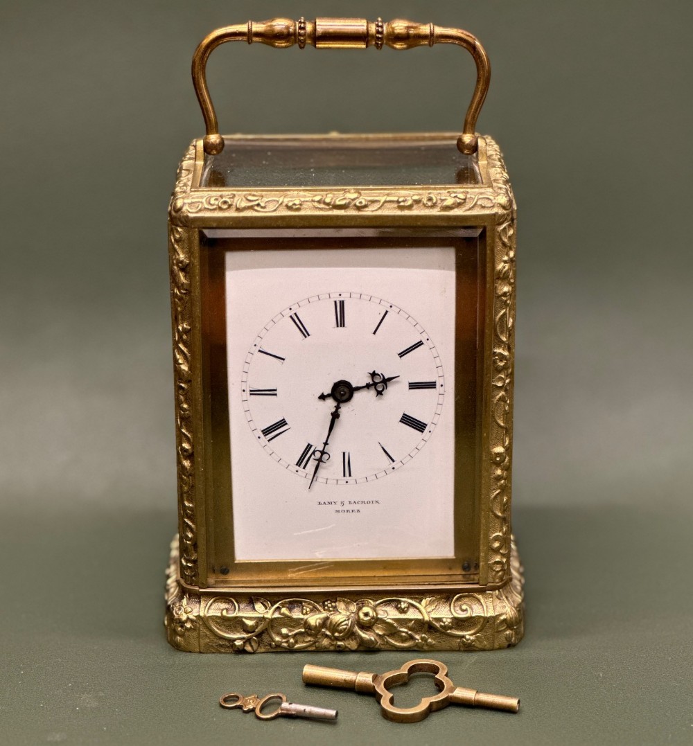 A 19th-century French gilt brass carriage clock featuring a relief foliate frame, clear glass sight panels, a white enamel dial with Roman numerals, and two winding keys.
