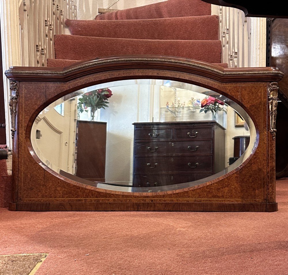 A late nineteenth-century horizontal burr yew-wood overmantel mirror featuring an oval bevelled glass plate, domed top rail, and gilt ormolu side mounts.