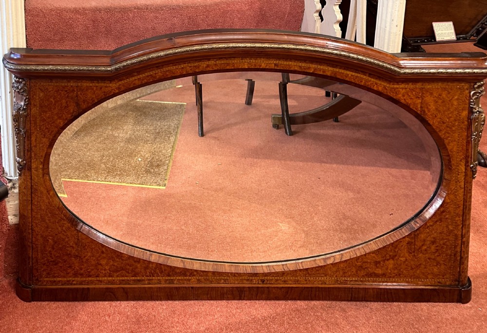 A late nineteenth-century horizontal burr yew-wood overmantel mirror featuring an oval bevelled glass plate, domed top rail, and gilt ormolu side mounts. View VI