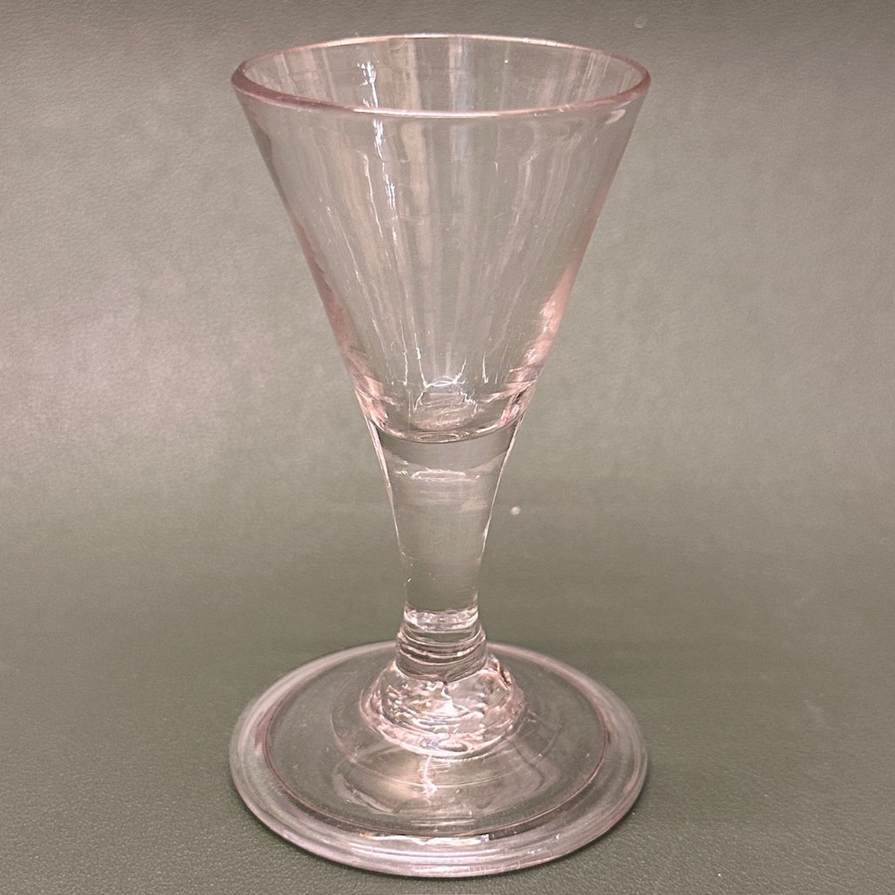 A clear blown glass dwarf ale glass with a conical bowl, short stem, and wide circular foot.