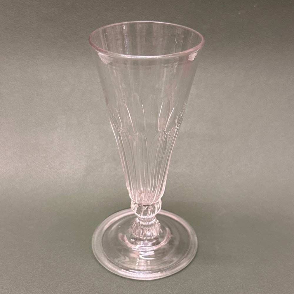 A clear Georgian lead glass ale glass featuring a tall conical bowl with lower wrythen fluting, supported on a short stem and circular flat foot.