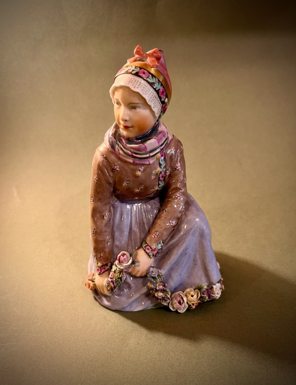 A set of ten hand-painted Royal Copenhagen porcelain figurines depicting seated children wearing traditional Danish regional costumes and floral garlands. View XI