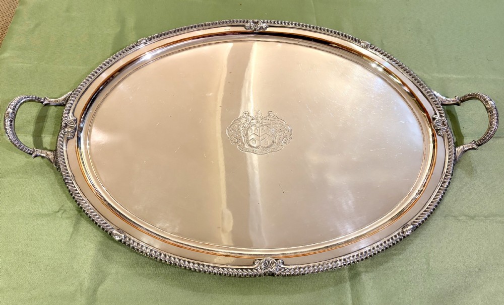 An oval Old Sheffield plate serving tray featuring two handles, a gadrooned rim with shell motifs, and an engraved armorial crest in the centre. View II