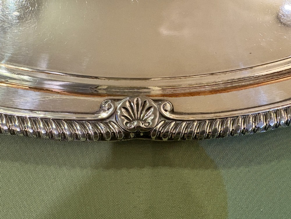 An oval Old Sheffield plate serving tray featuring two handles, a gadrooned rim with shell motifs, and an engraved armorial crest in the centre. View III