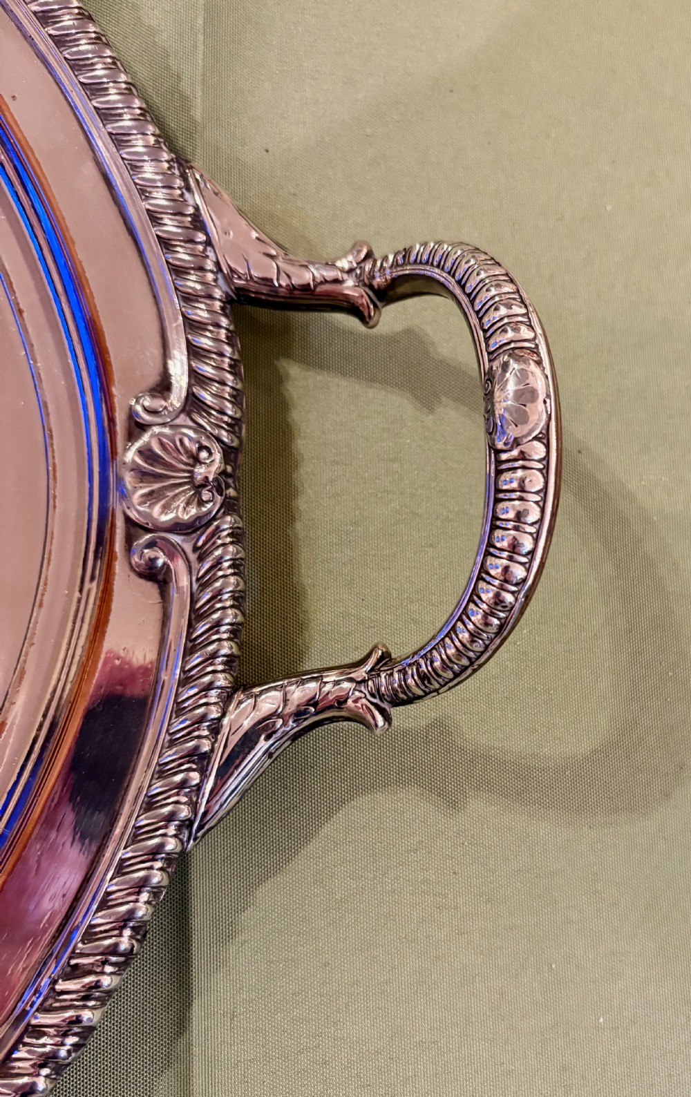 An oval Old Sheffield plate serving tray featuring two handles, a gadrooned rim with shell motifs, and an engraved armorial crest in the centre. View V