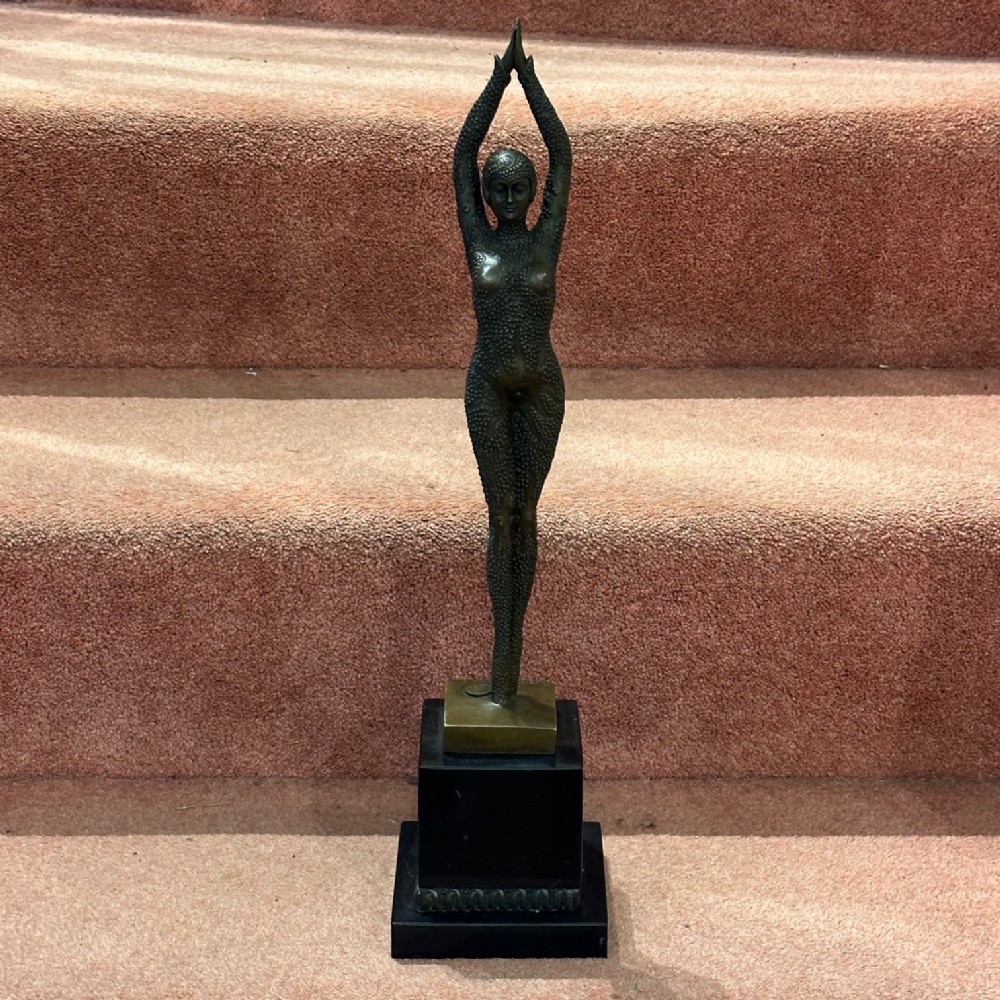 An Art Deco bronze figure depicting a standing female dancer with raised arms and a textured bodysuit, set upon a tiered black marble base.