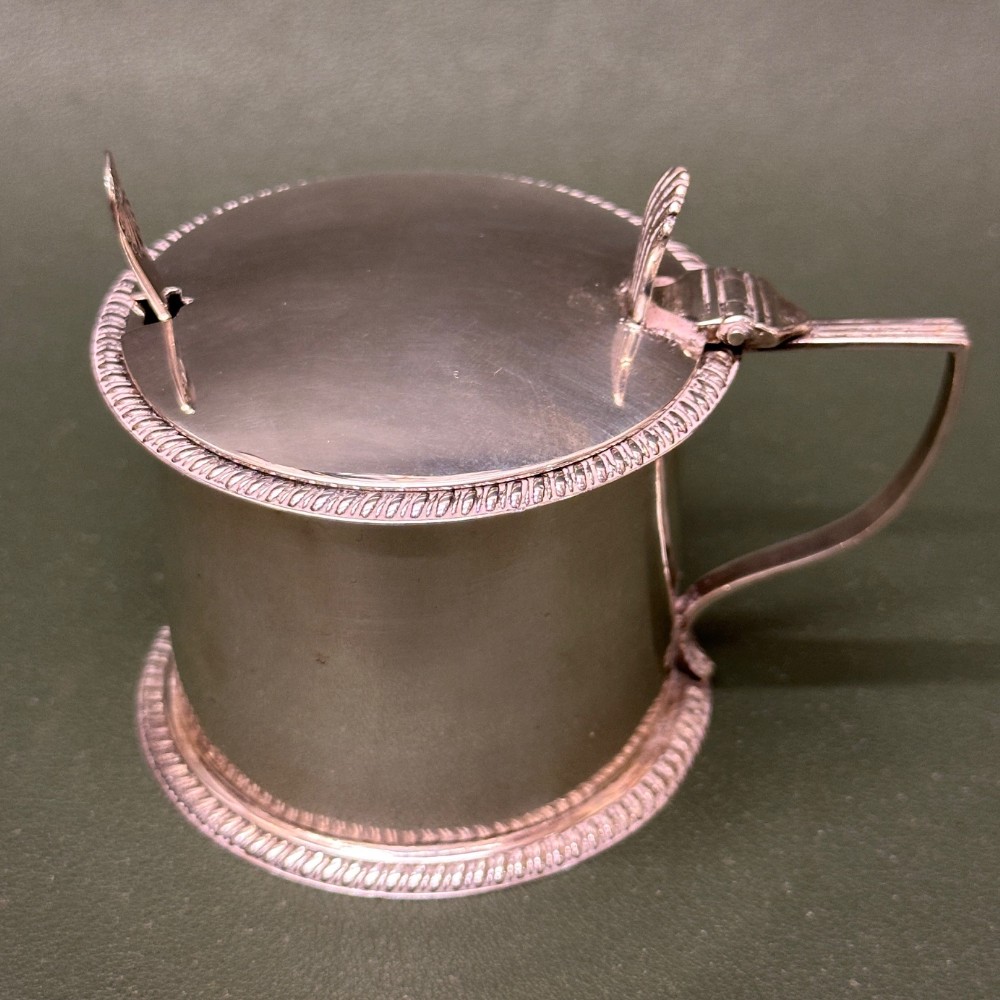 An antique sterling silver mustard pot featuring a cylindrical body, hinged lid, integrated handle, and rope-twist decorative borders.