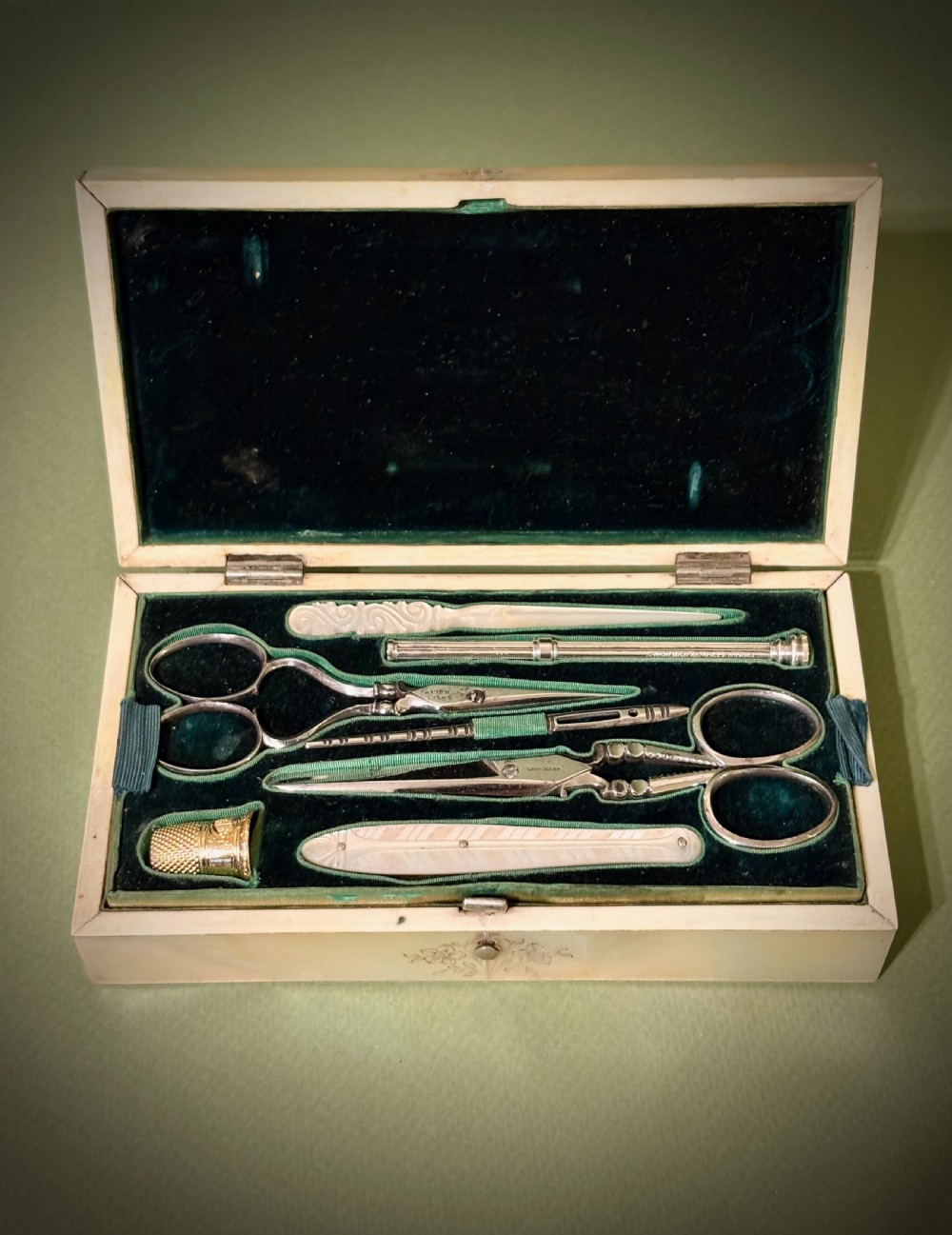 An open rectangular mother-of-pearl sewing box lined with deep green velvet, featuring a removable tray filled with fitted metal and nacre needlework tools. View III