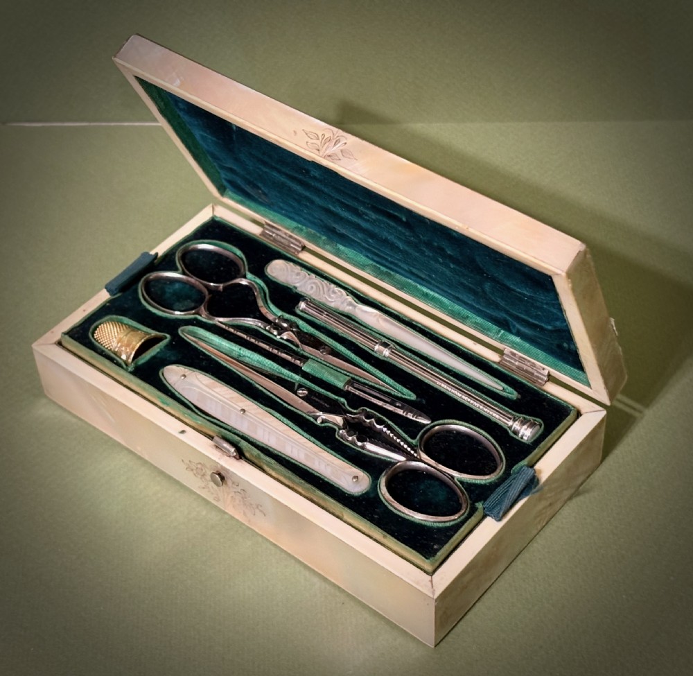 An open rectangular mother-of-pearl sewing box lined with deep green velvet, featuring a removable tray filled with fitted metal and nacre needlework tools. View IV