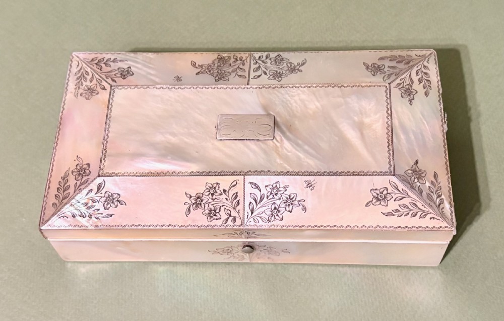 An open rectangular mother-of-pearl sewing box lined with deep green velvet, featuring a removable tray filled with fitted metal and nacre needlework tools. View V