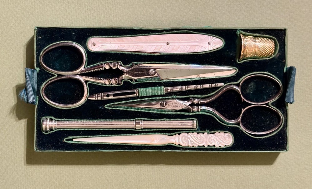 An open rectangular mother-of-pearl sewing box lined with deep green velvet, featuring a removable tray filled with fitted metal and nacre needlework tools. View VI